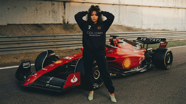 Person in a black outfit standing next to a red Formula 1 car on a track.